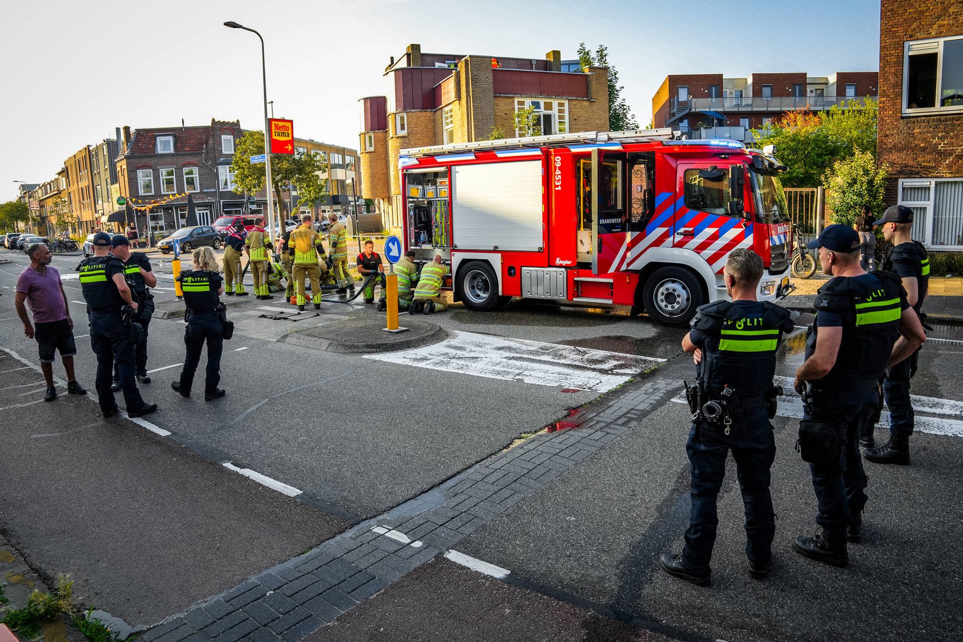 Emergency responders and a red fire truck on a city street, with police officers and bystanders watching a rescue operation.