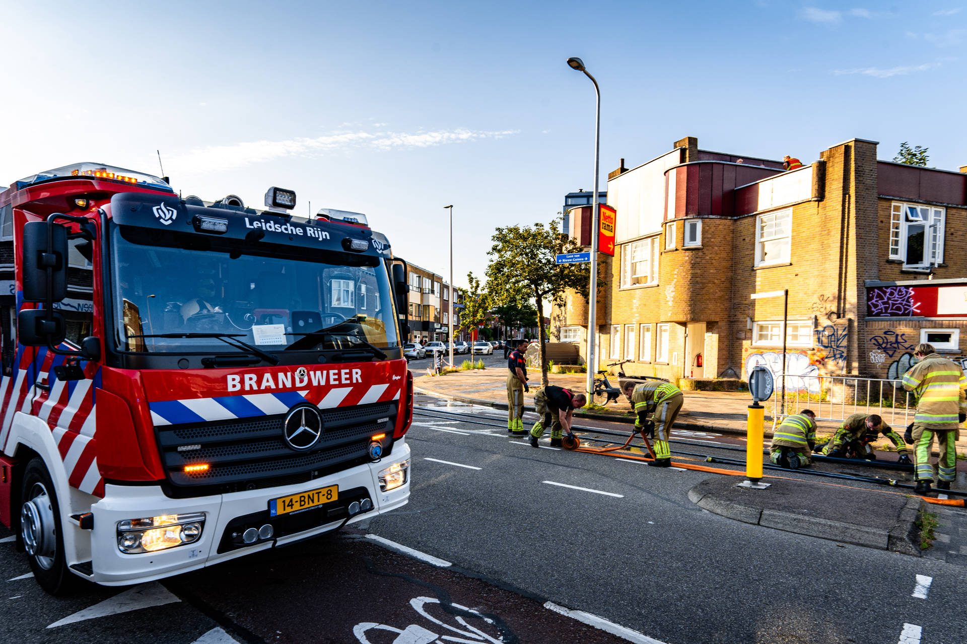 Fire brigade truck on a city street with firefighters connecting hoses and working at the scene.