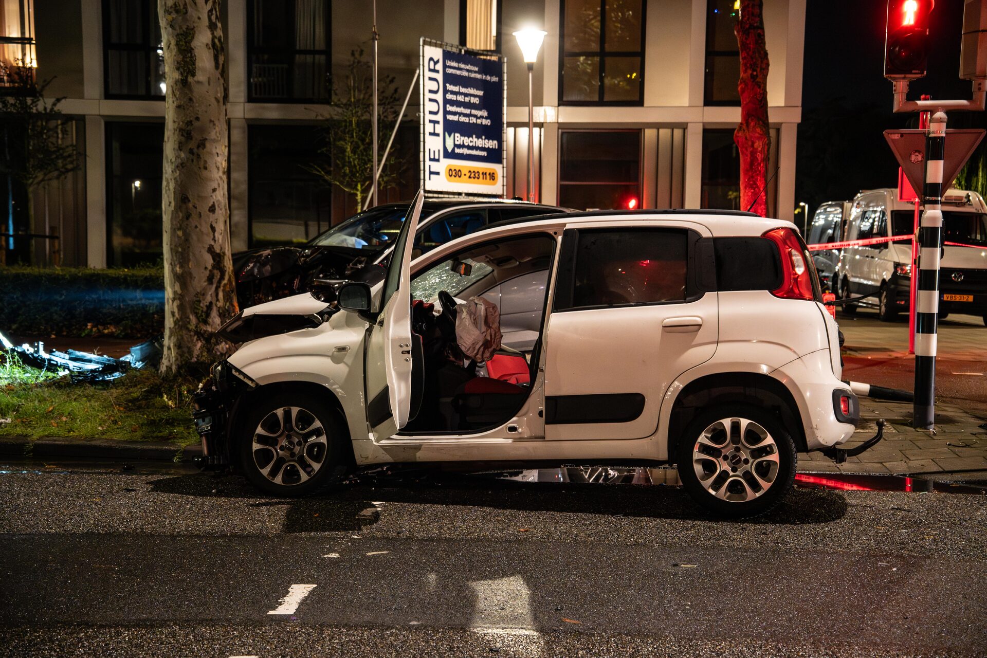White SUV with extensive front-end damage and the doors open after a nighttime collision on a city street.
