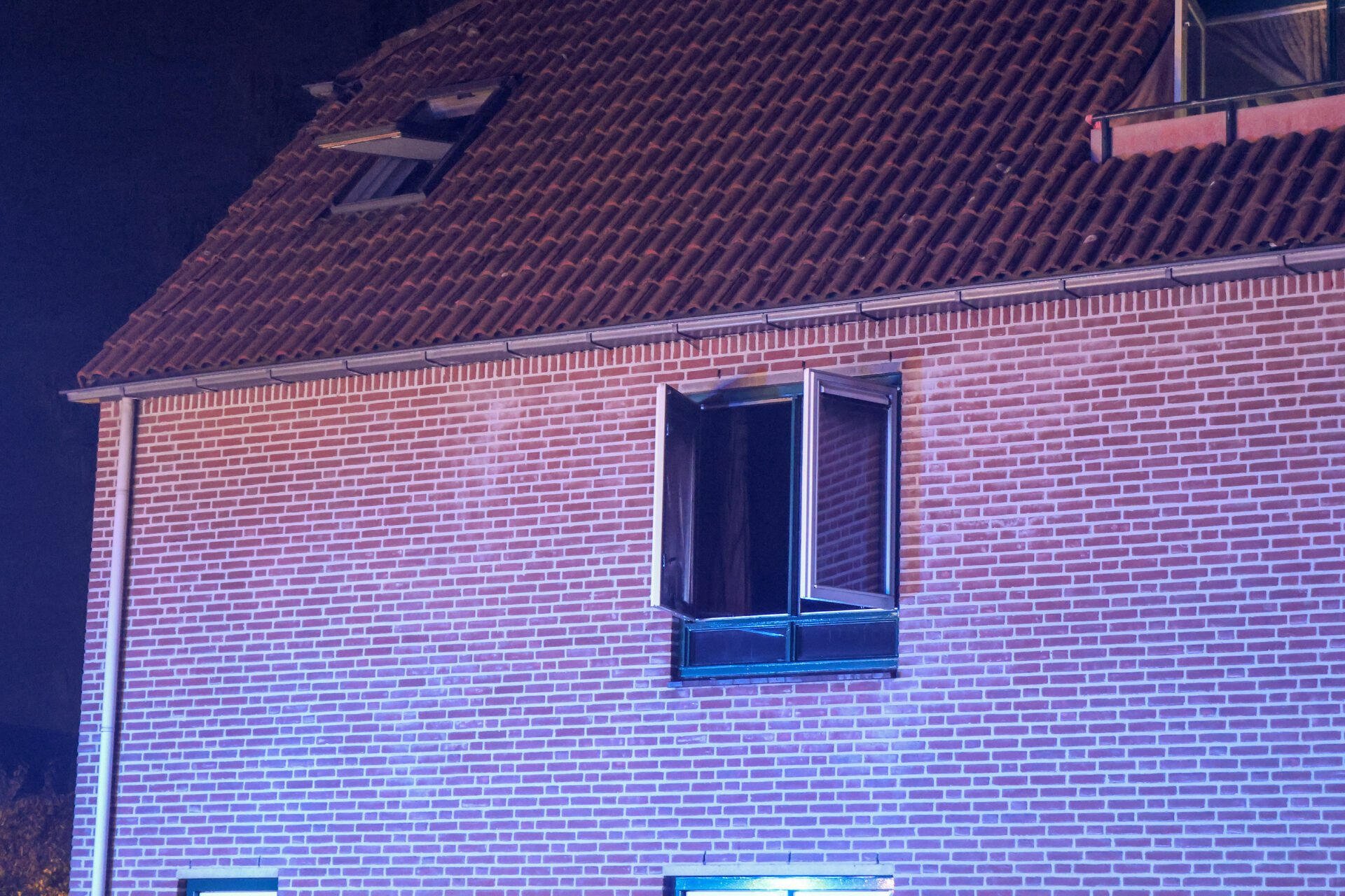 Brick building at night with a sloped tiled roof and a small balcony on the upper floor.