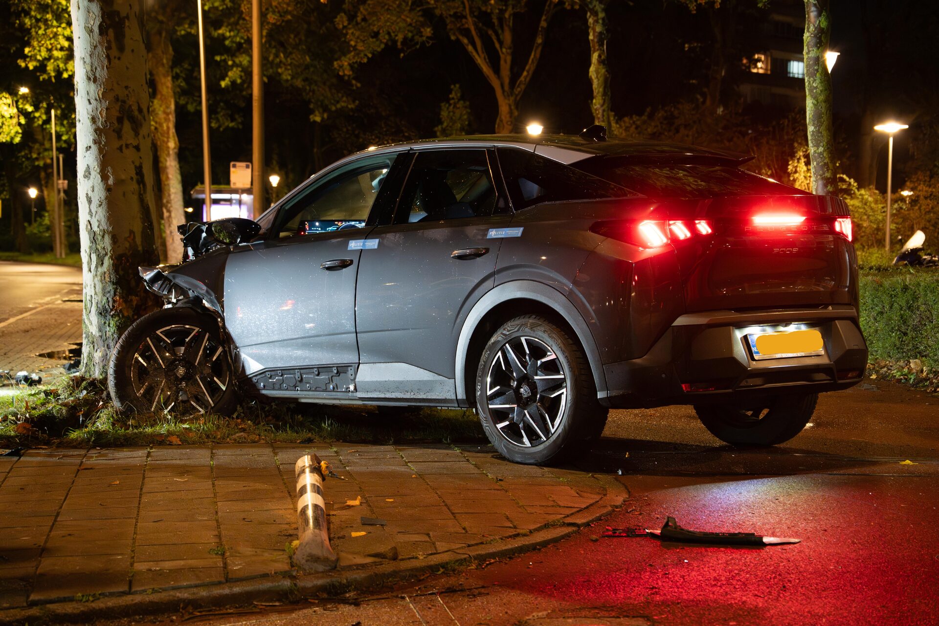 Nighttime car crash: a silver SUV with a crushed front left side, hitting a tree, debris on the sidewalk.