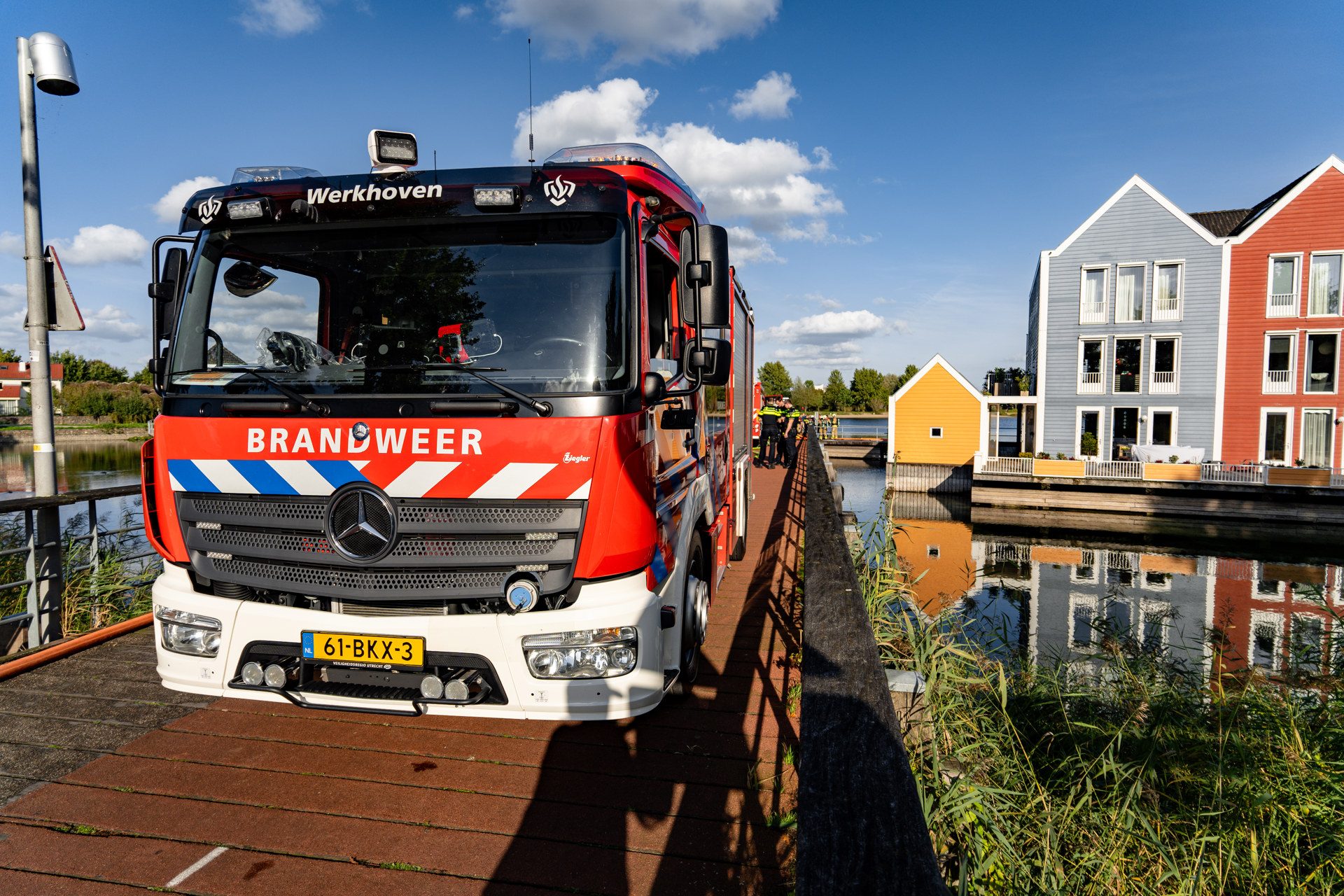 Red fire truck parked on a wooden boardwalk by water with colorful houses in the background.