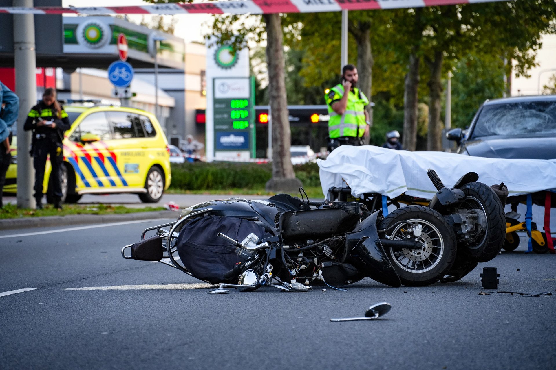 Motorcycle crash scene with toppled bikes, police officer on the scene and emergency tape in a city street.
