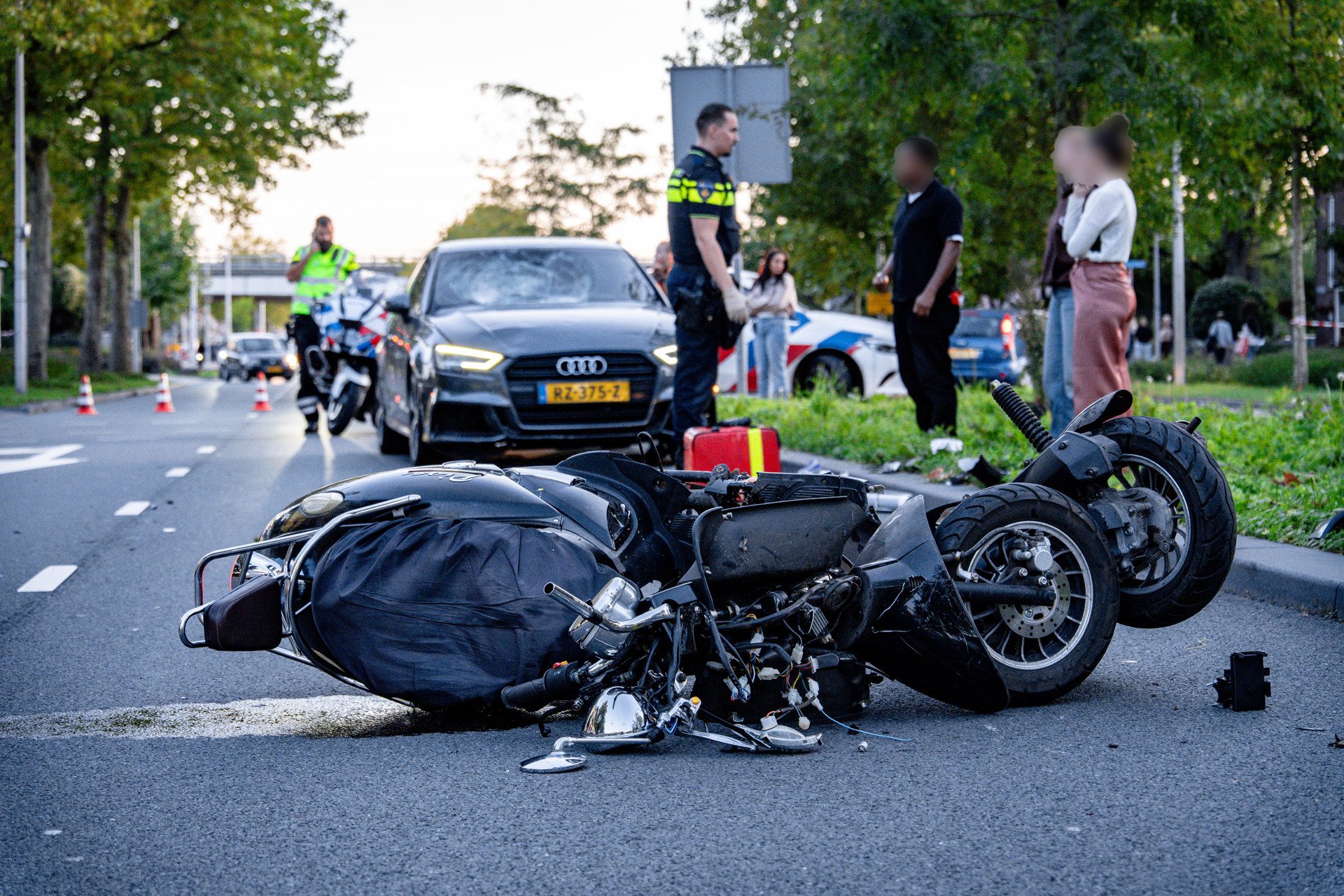 Motorcycle crash on city street with debris, lying on its side; police and bystanders in the background.