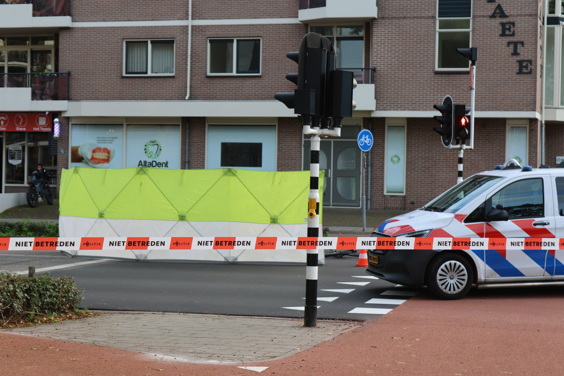 Construction barriers block a city street at a construction site, with a police van, traffic lights, and Niet Betreden tape across the road.