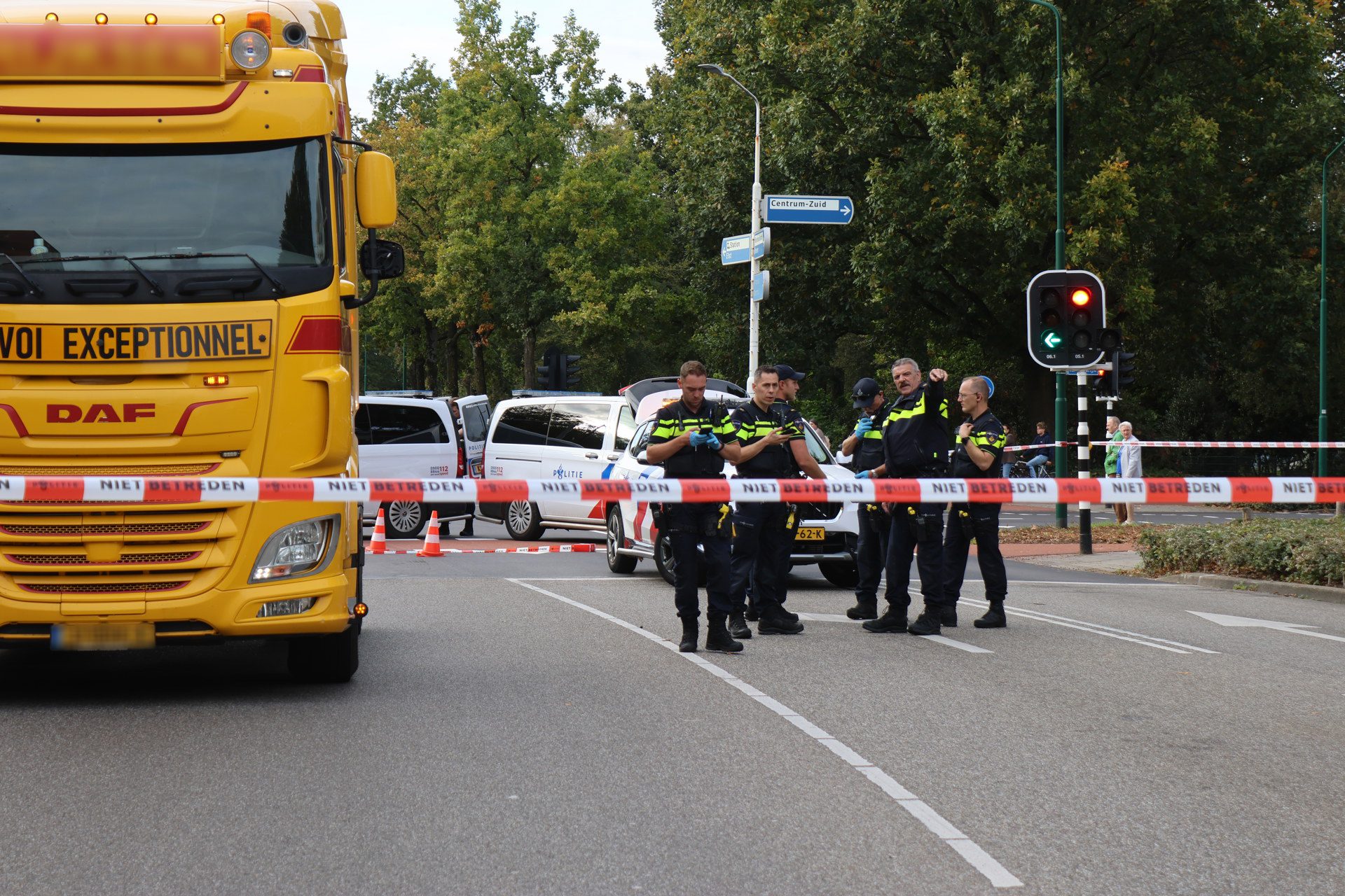 Large yellow bus at left blocking the road as police stand nearby behind red-and-white 'do not enter' tape