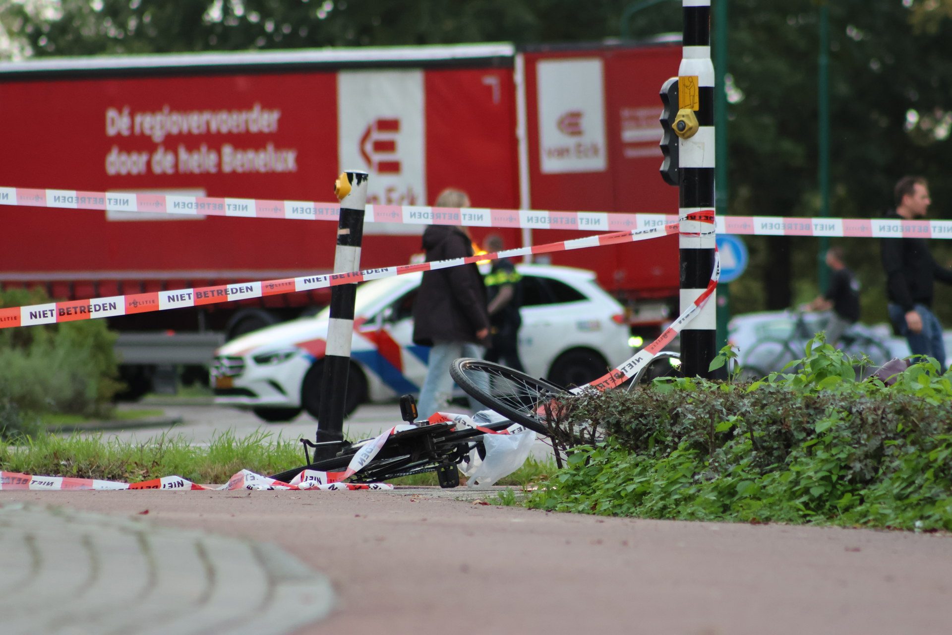 A fallen bicycle lies by the curb, taped off with 'NIET BETREDEN' signs and red emergency trucks in the background.