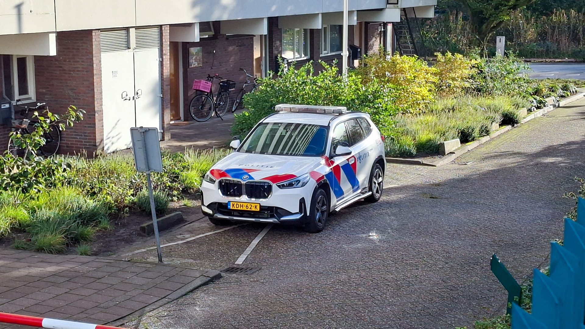 White Dutch police SUV parked on a cobblestone street beside a residential building, with bicycles and greenery nearby.