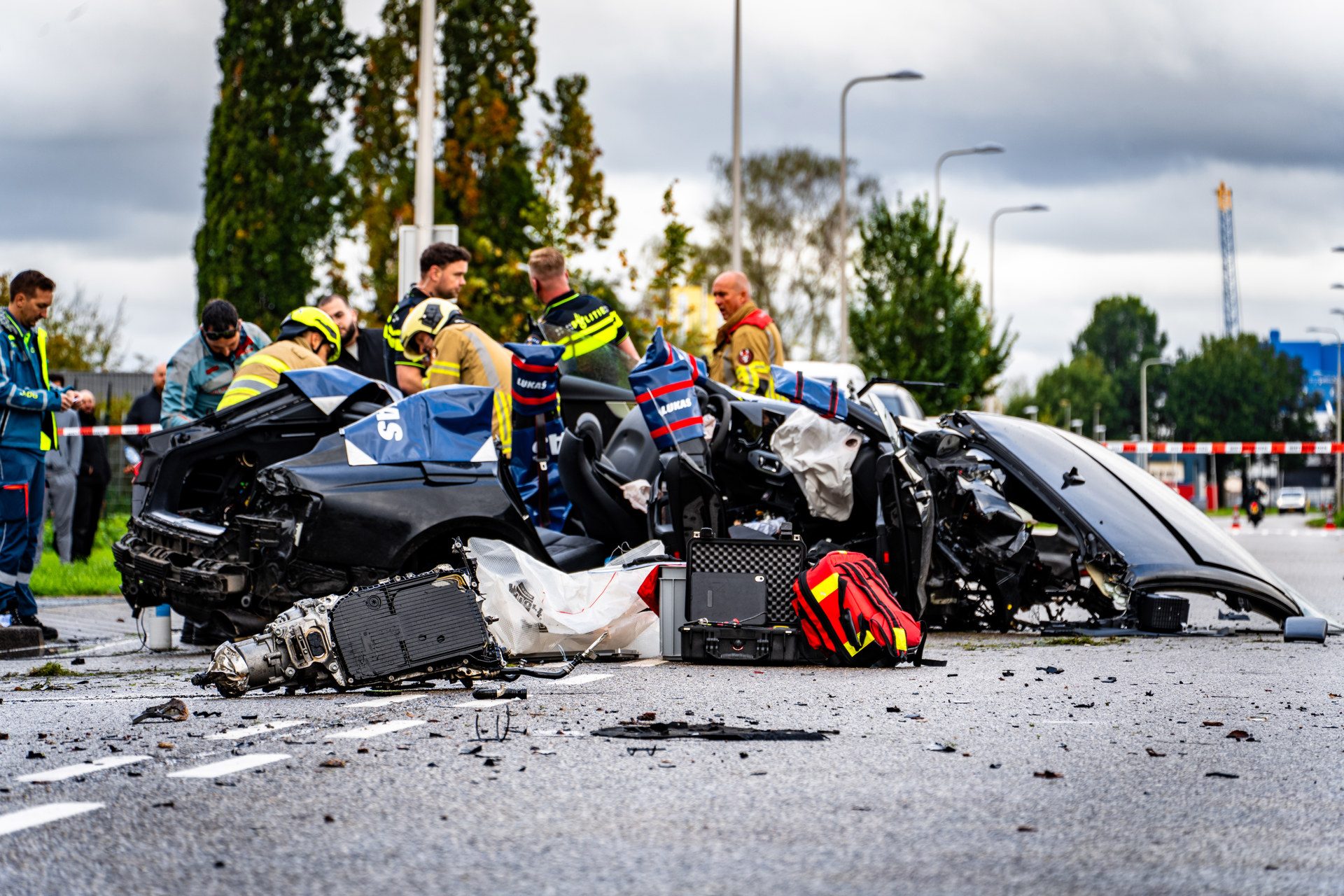 Emergency responders assess a severely damaged car at a high-speed crash scene with debris all around.