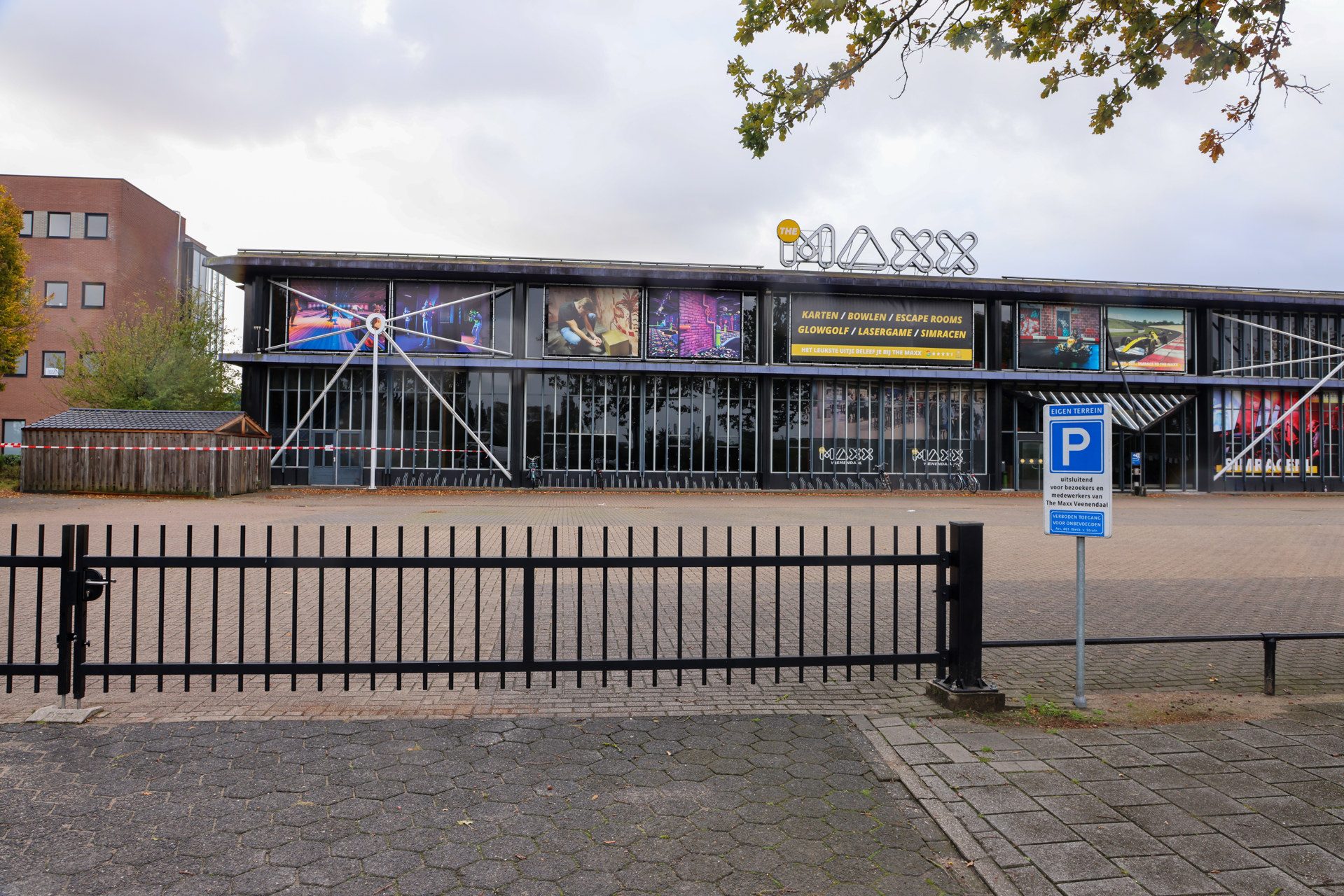 Exterior view of a modern entertainment venue with The Maxx sign on the roof, large display windows, and a metal fence in the foreground