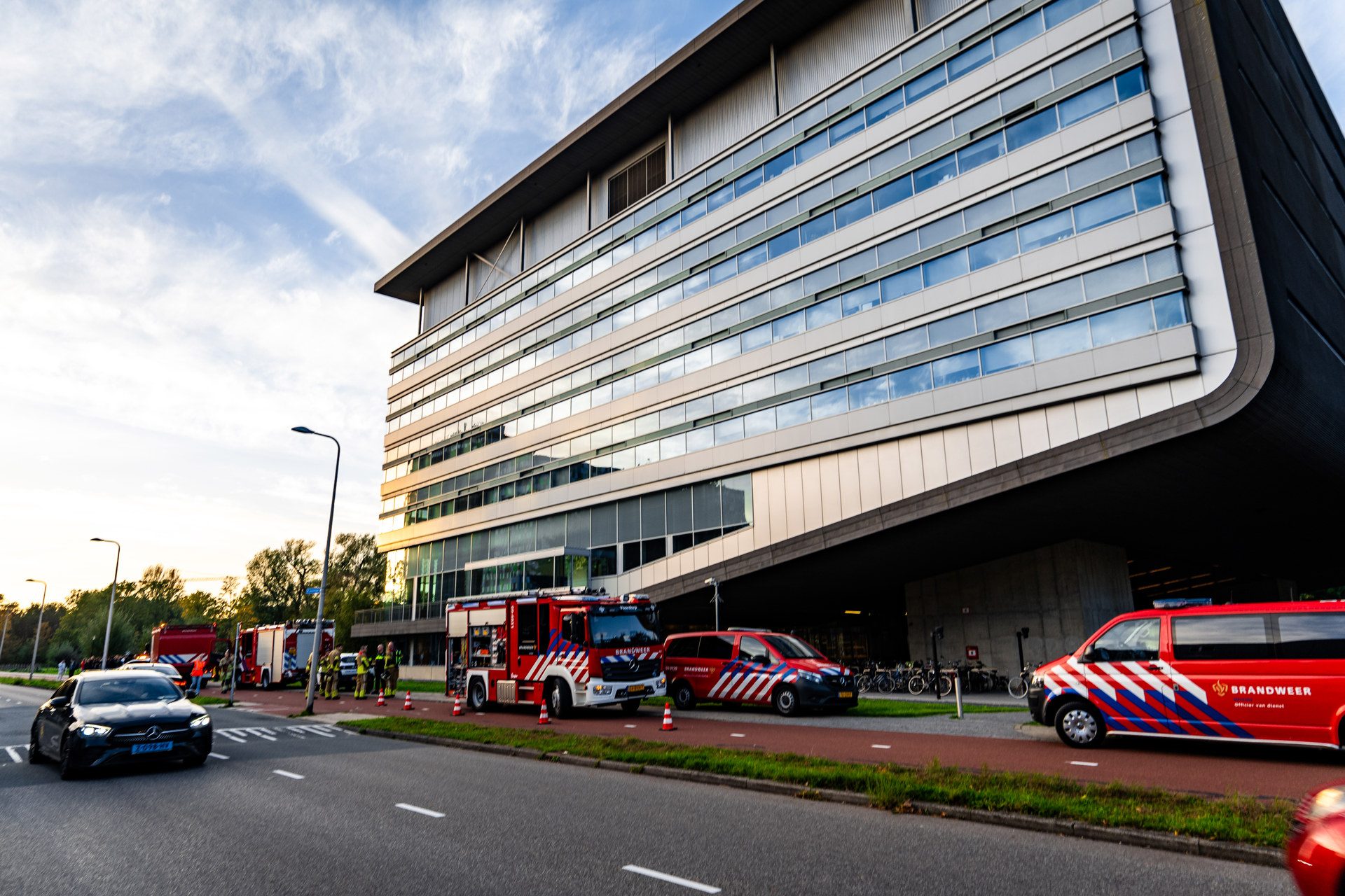 Firefighters and red emergency vehicles parked outside a modern office building.